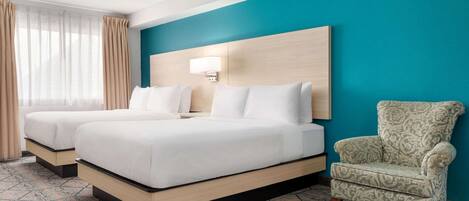 Habitación de hotel con dos camas, un sillón estampado y una pared de acento color verde azulado.