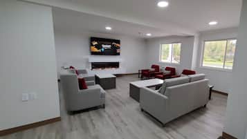 A modern living room with a flat-screen TV, grey sofas, red chairs, and a fireplace.