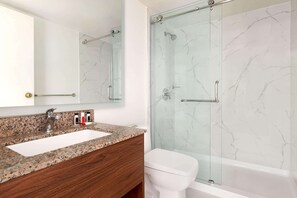 A bathroom with a granite countertop sink, a mirror, a glass shower enclosure, and a white toilet.