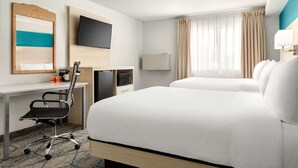 Quarto de hotel com uma cama, uma escrivaninha com cadeira, televisão, micro-ondas e janela com cortinas.