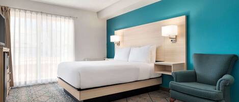 Una habitación de hotel con cama, una silla, una mesita de noche y una lámpara de pared.