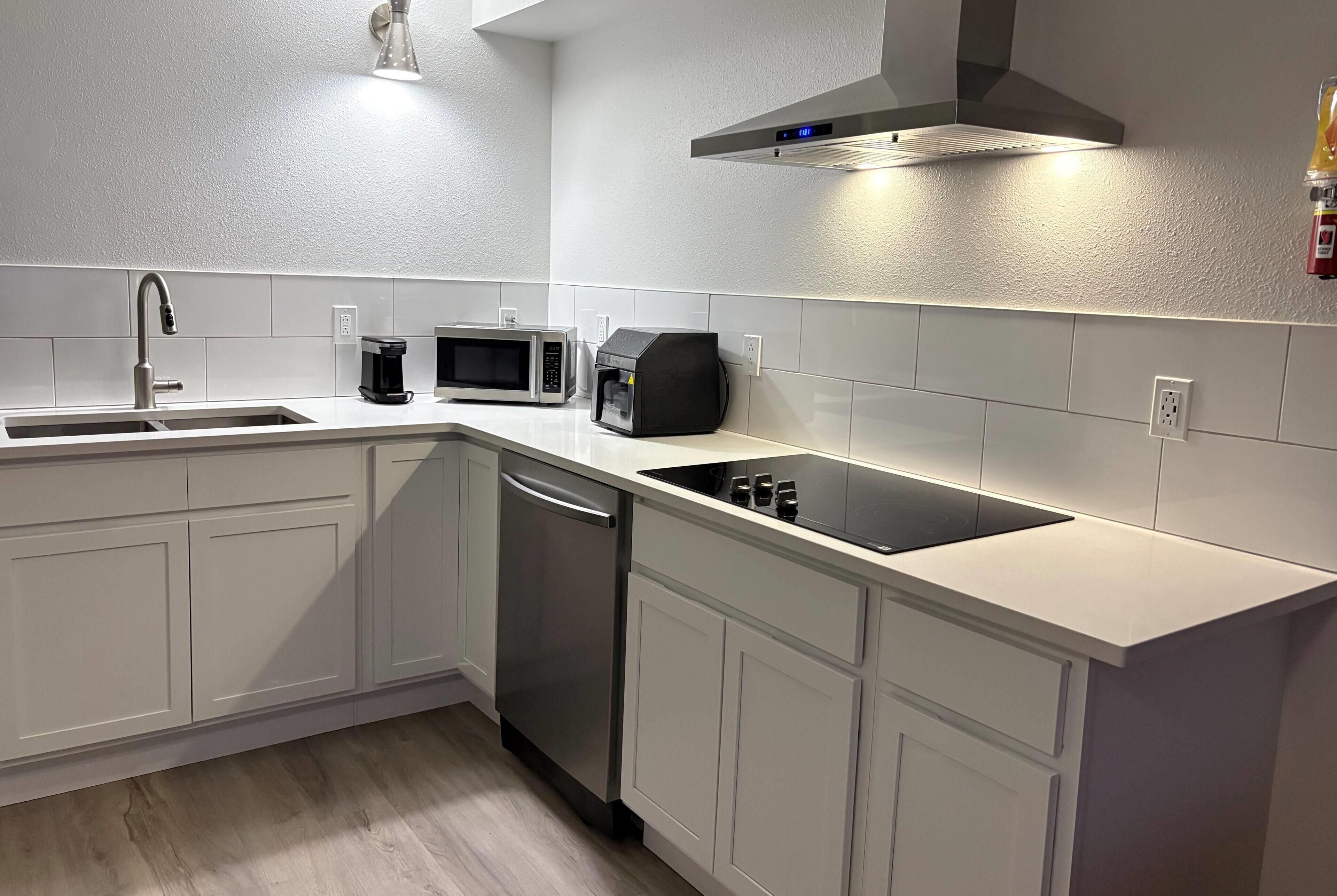 A modern kitchen with white cabinetry, a stainless steel dishwasher, a microwave, and a coffee maker.