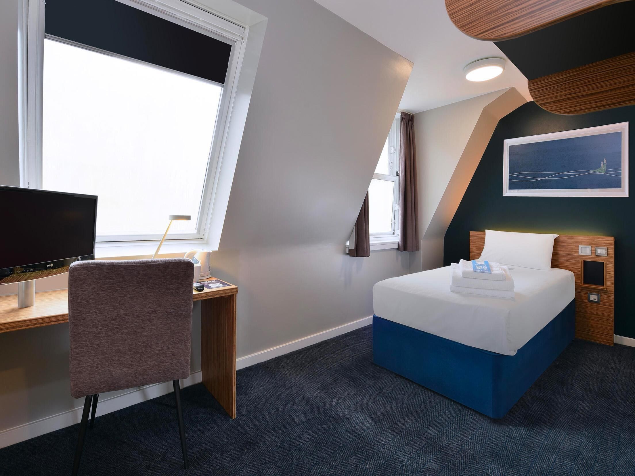 Ein Hotelzimmer mit Bett, Schreibtisch, Stuhl und einem großen Fenster.