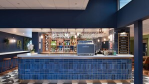 A bar area with a blue tiled counter, a menu board listing drinks, and a bar stocked with bottles. - Travelodge London Covent Garden (London)