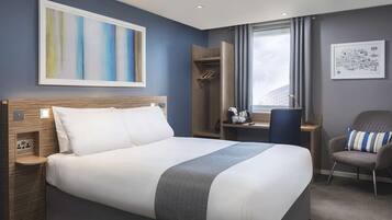 A modern hotel room with a large bed, a desk, a chair, and a window with a cityscape view.