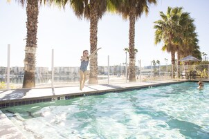A swimming pool with a view of a cityscape, surrounded by palm trees and a fence.