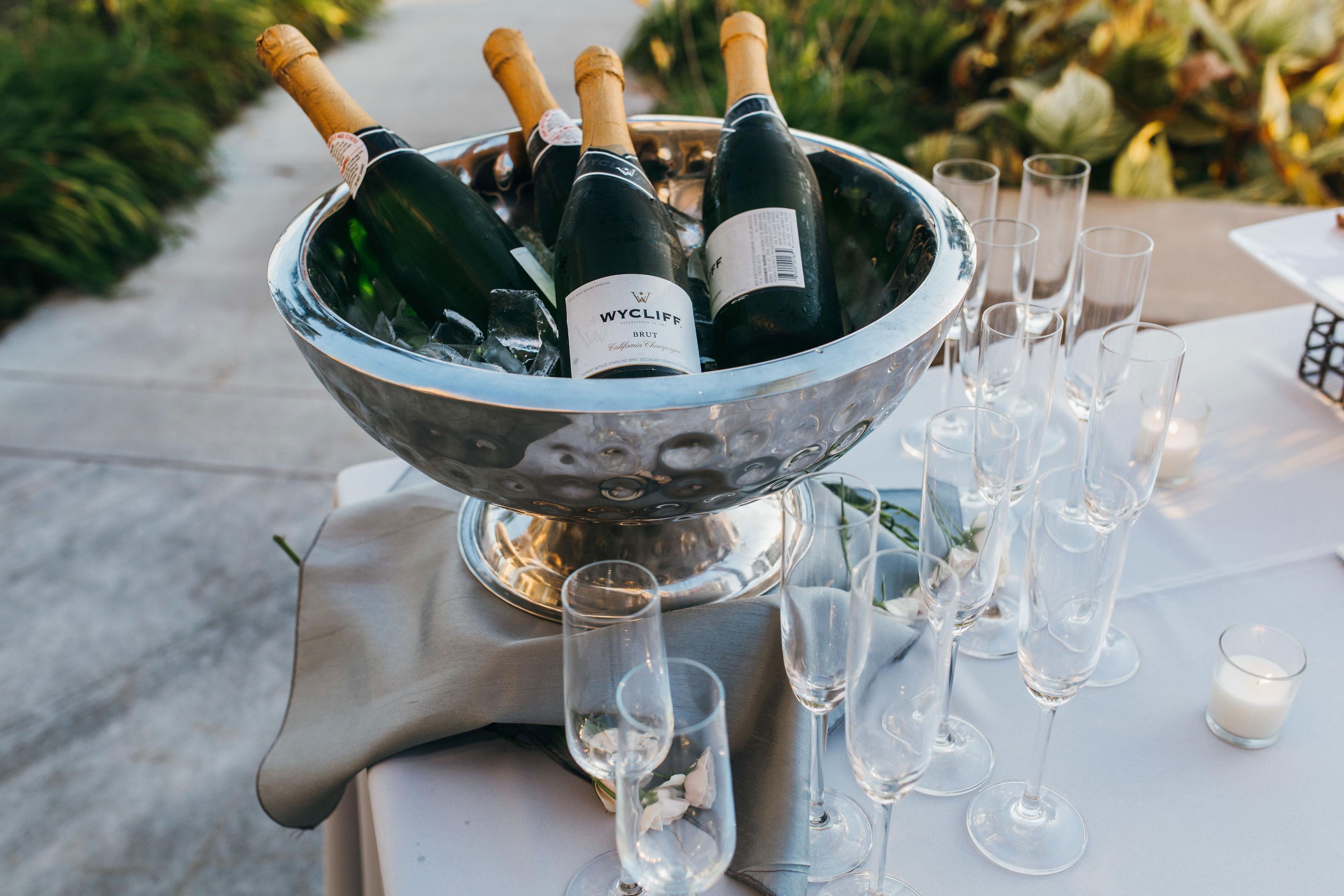 Un seau à glace en argent rempli de bouteilles de vin et de verres, posé sur une table.