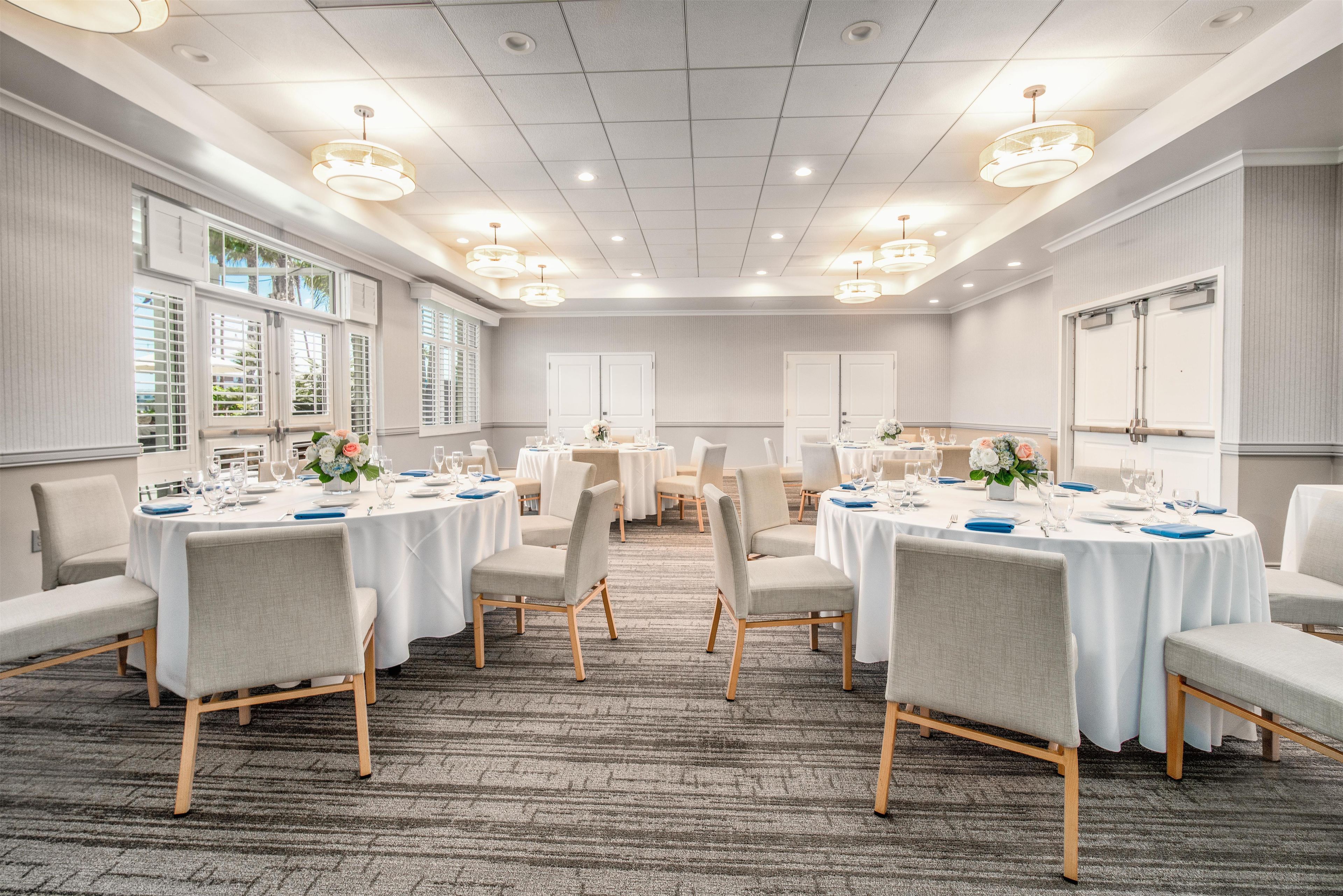 A hotel conference room with round tables, chairs, and a carpeted floor.