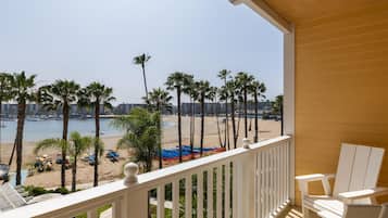 Un balcón con vista a una playa, palmeras y un puerto deportivo.