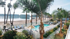 Ein Poolbereich mit Liegestühlen und Sonnenschirmen, umgeben von Palmen und Blick auf den Strand.
