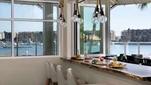 Ein Essbereich mit Blick auf eine Marina, ausgestattet mit einem langen Tisch mit Stühlen, einer Theke und einer Hängeleuchte.