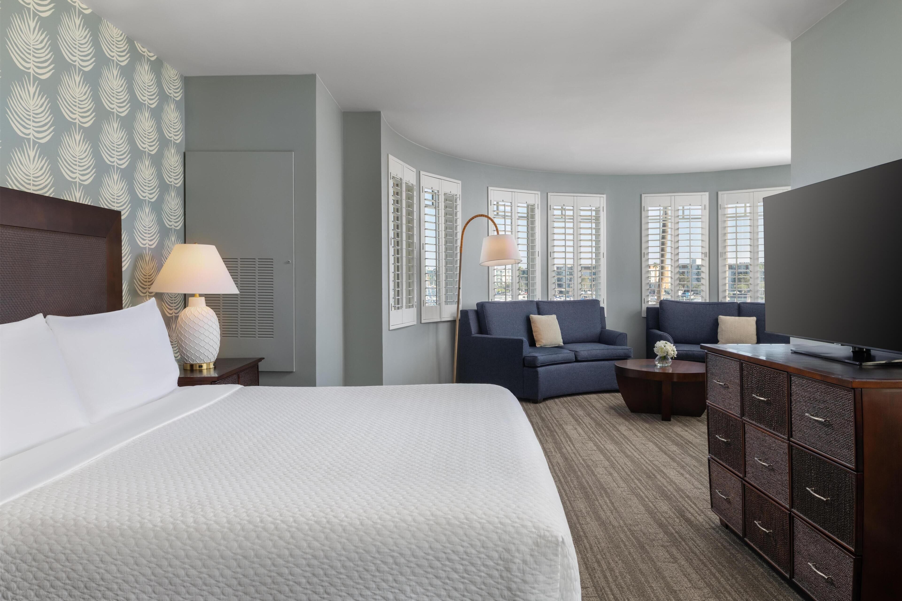 A hotel room with a bed, two sofas, a TV, a dresser, and a lamp.