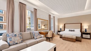 A modern hotel room with a sofa, a desk, a chair, a bed, and a nightstand.