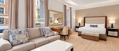 A modern hotel room with a sofa, a desk, a chair, a bed, and a nightstand.