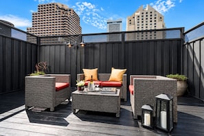 An outdoor seating area with wicker furniture and red cushions, a bottle of wine, and a candle on a wooden deck. - Hotel Union Square (San Francisco)