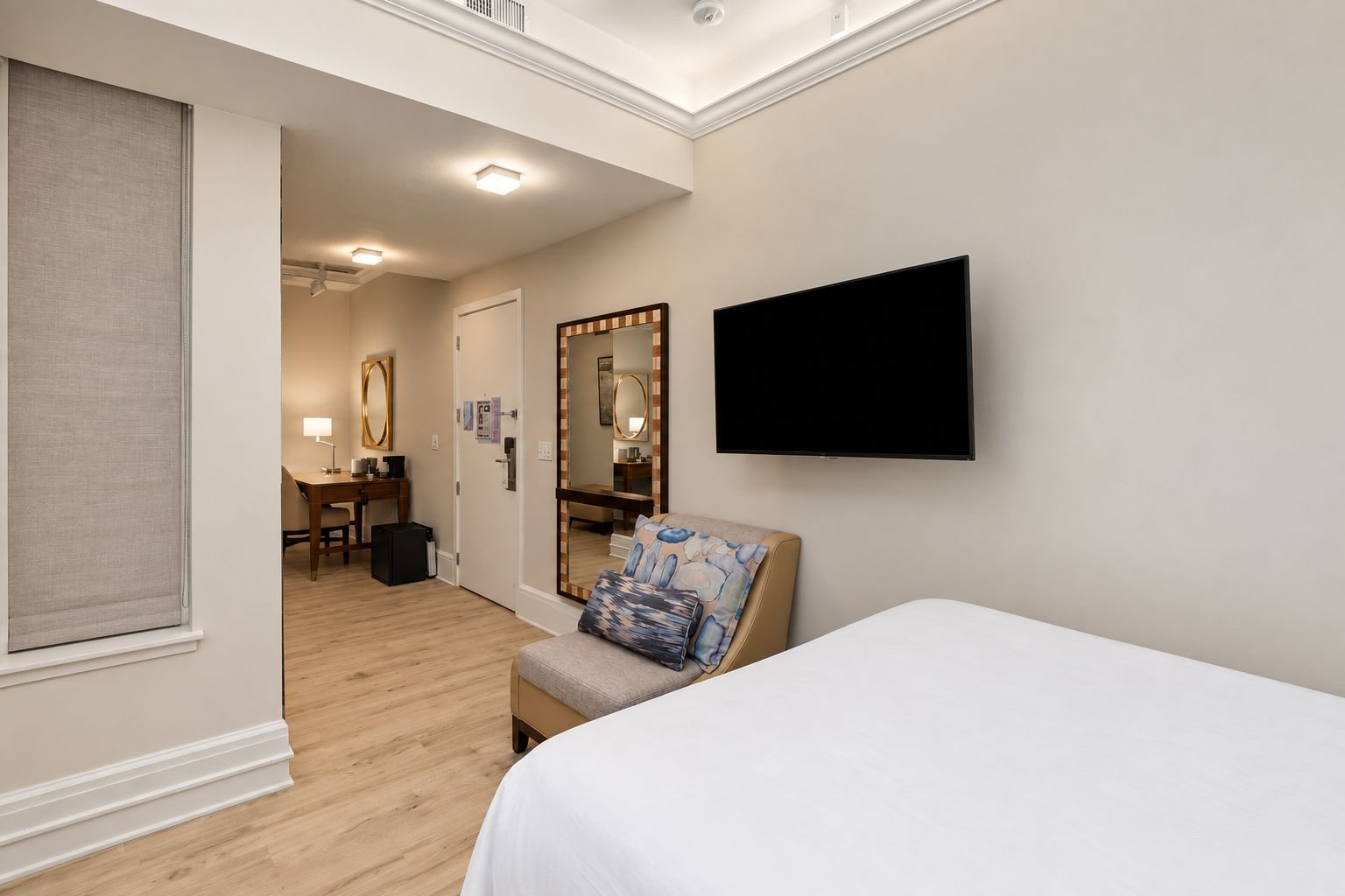 Een hotelkamer met een bed, een aan de muur bevestigde televisie, een bureau met een stoel, en een grote spiegel.
