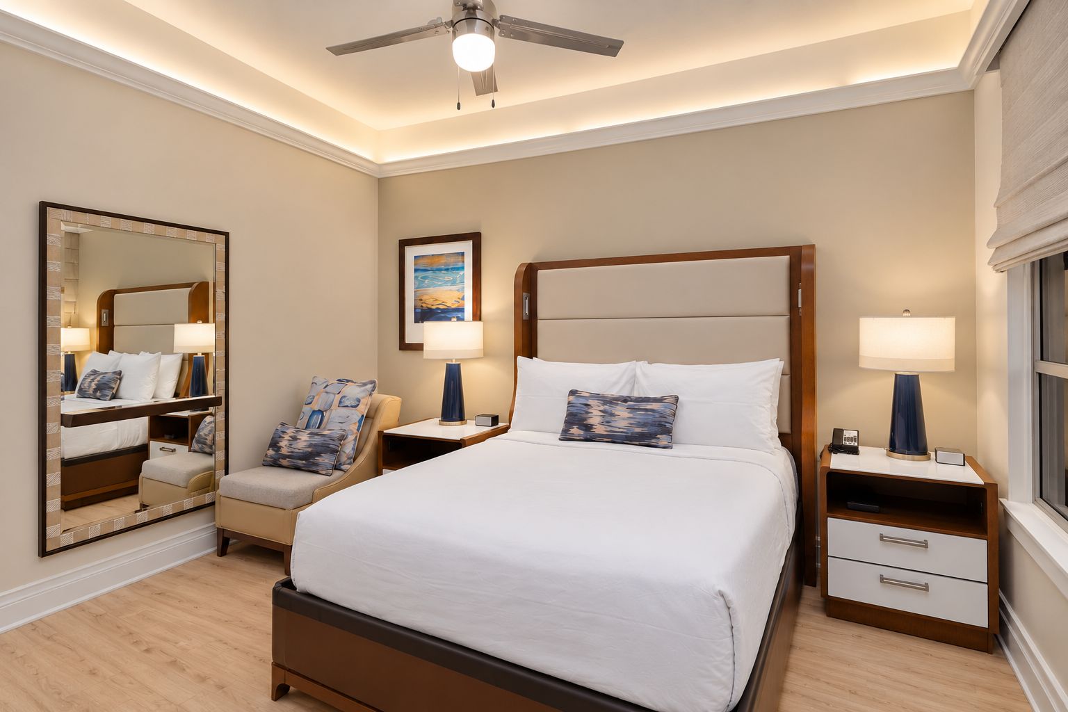 A hotel room with a bed, bedside tables, a chair, a mirror, and a ceiling fan.