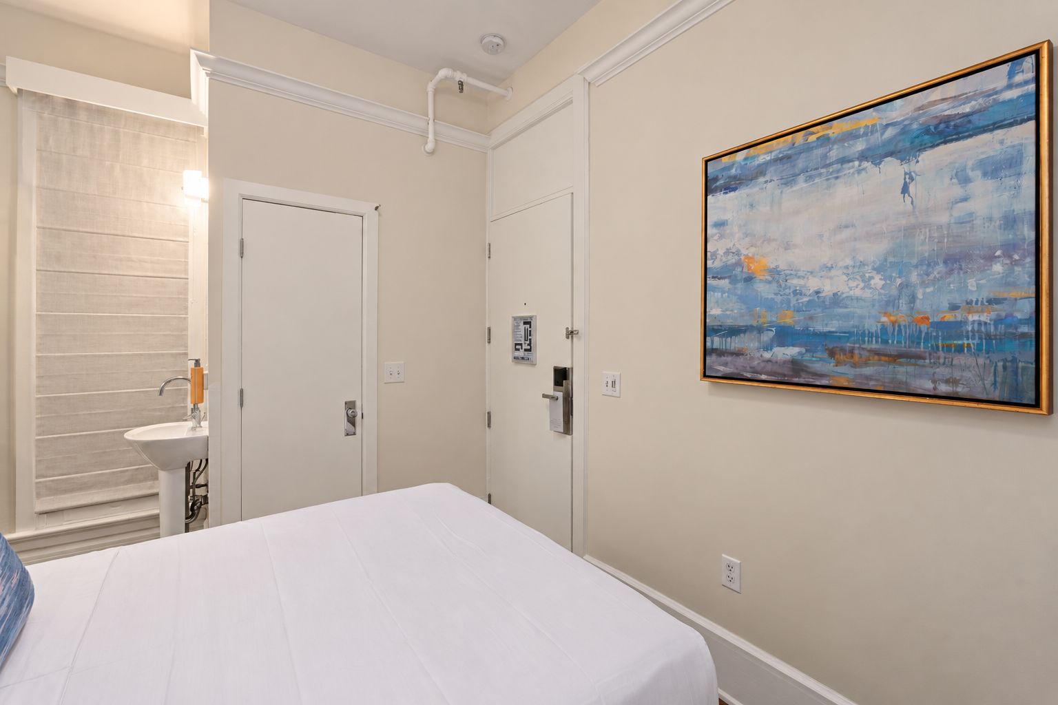 A hotel room with a bed, a bathroom with a sink, and a painting on the wall.