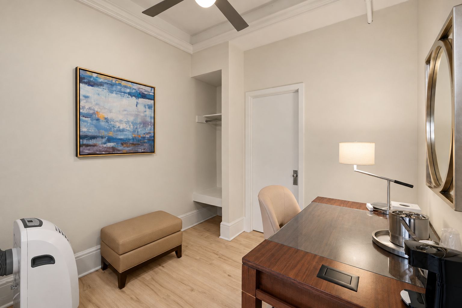 A hotel room with a wooden dining table, a bench, a painting, a lamp, and a coffee machine.
