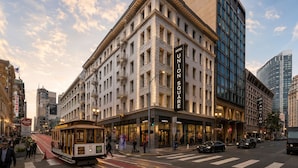 Un edificio histórico con un cartel llamativo que dice 'Hotel Union Square', una línea de tranvía y una concurrida calle urbana.