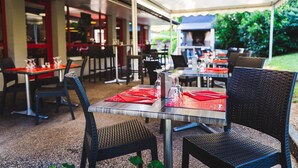 An outdoor dining area with tables and chairs, covered by a canopy.