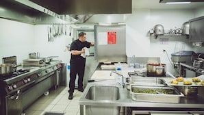 A commercial kitchen with stainless steel appliances, a chef preparing food, and various cooking utensils and ingredients.