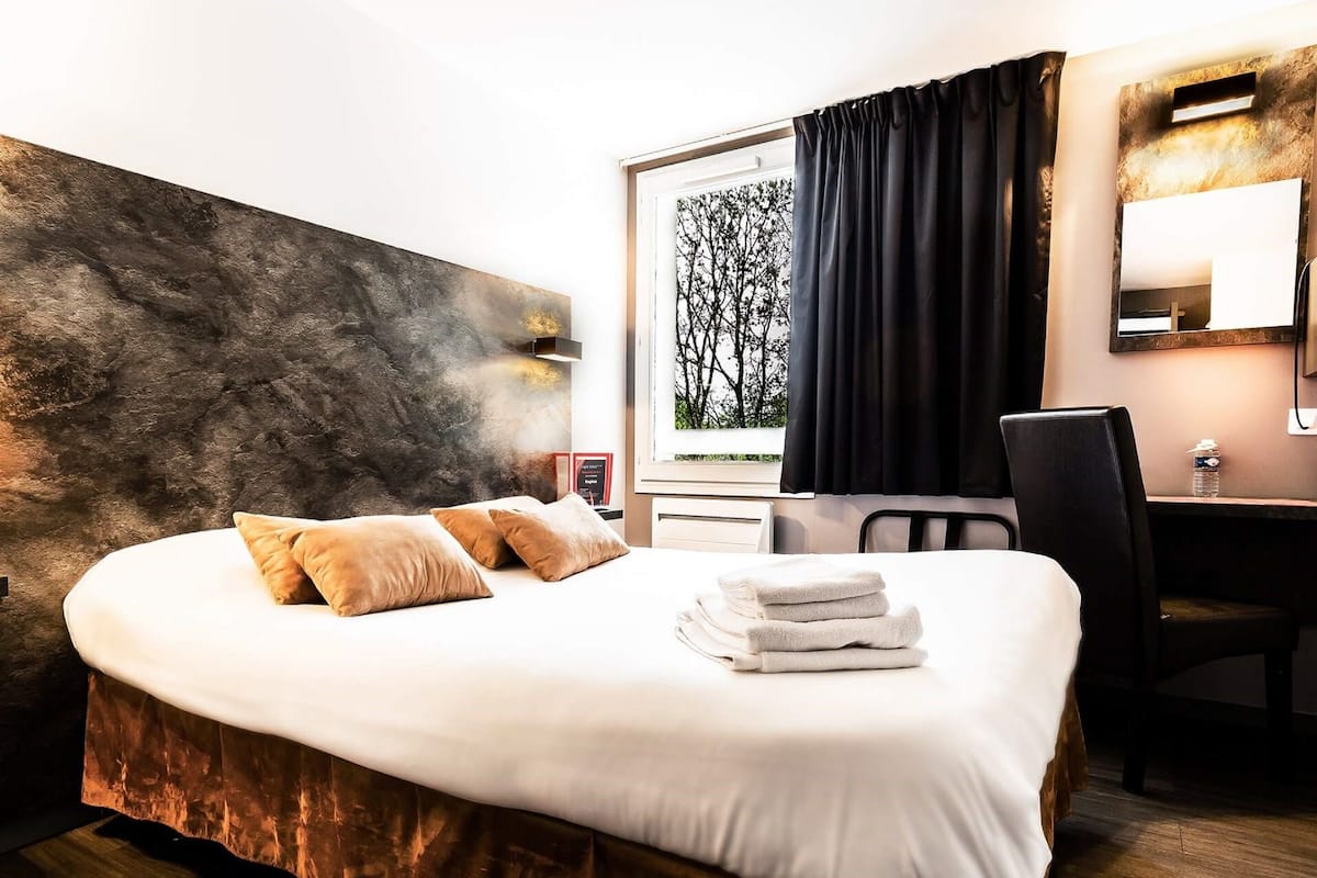 A hotel room with a large bed, a desk, and a window with curtains.
