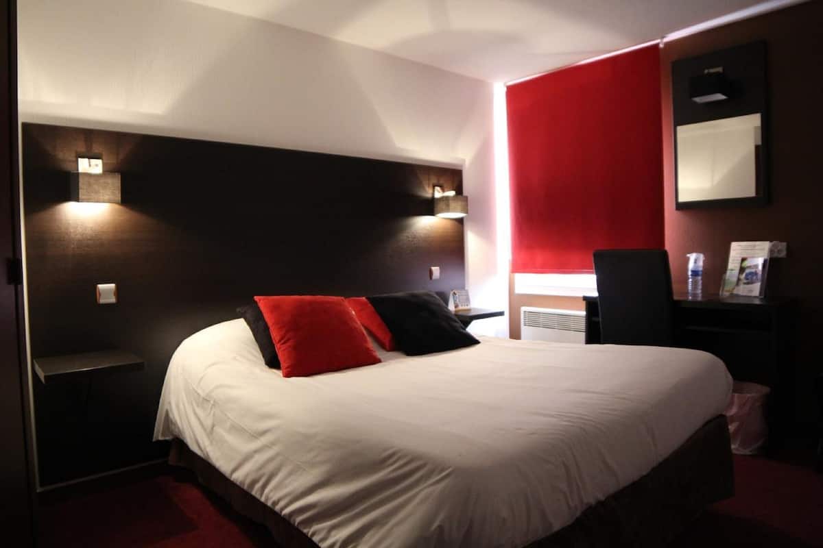 A hotel room with a bed, bedside tables, a desk, and a chair.