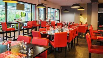 A restaurant with red chairs and tables, large windows, and hanging pendant lights.