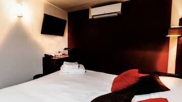 Une chambre d’hôtel avec un lit bien fait, un bureau avec une lampe, un téléphone et un appareil de climatisation fixé au mur.
