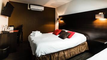 A hotel room with a bed, a desk, a chair, an air conditioning unit, and a wall-mounted light fixture.