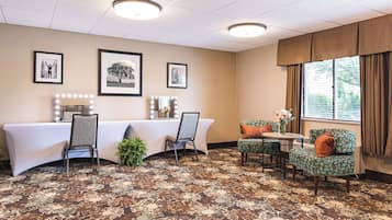 A hotel room with a large table, two chairs, a small round table, and a window with curtains.