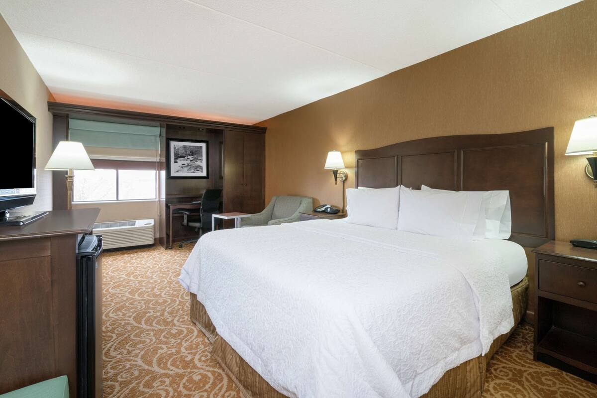A hotel room with a large bed, two bedside lamps, a desk with a lamp, a chair, and a television.