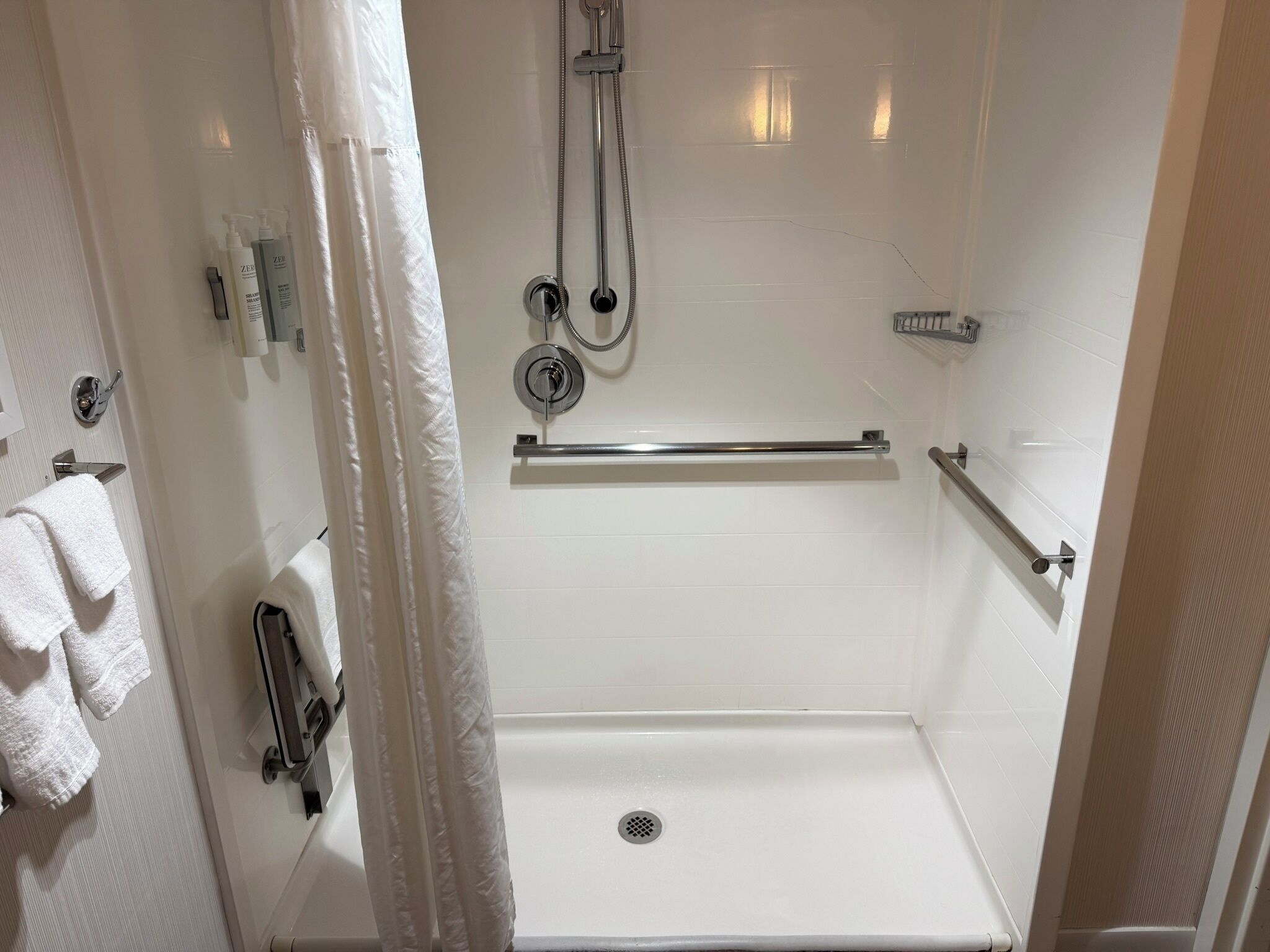 A shower area with a white bathtub, grab bars, a handheld showerhead, and a towel rack with towels.