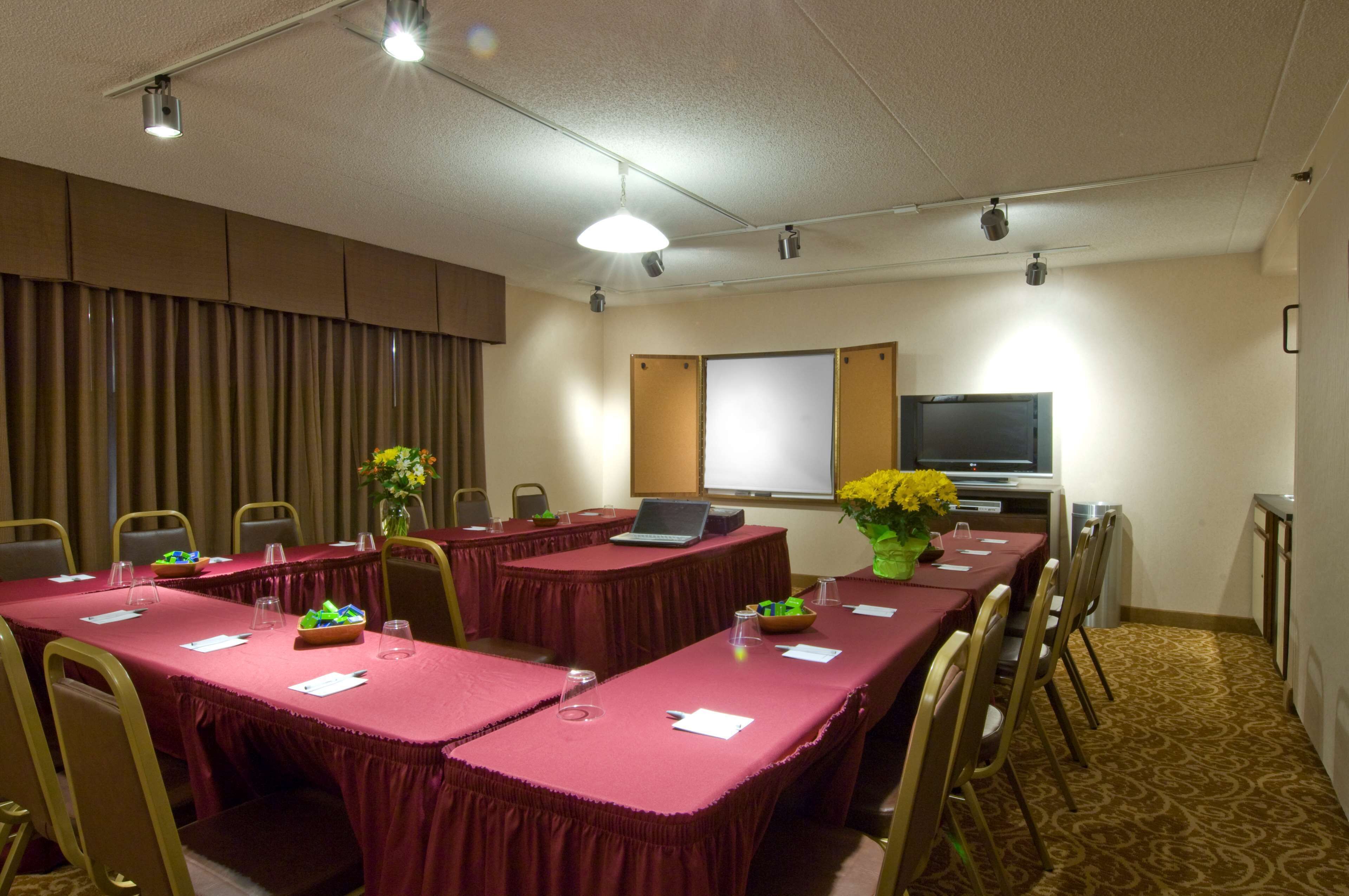 Uma sala de conferências com uma mesa comprida, cadeiras, um laptop e uma tela de projeção.