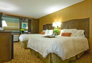 A hotel room with two beds, a desk, and a lamp.