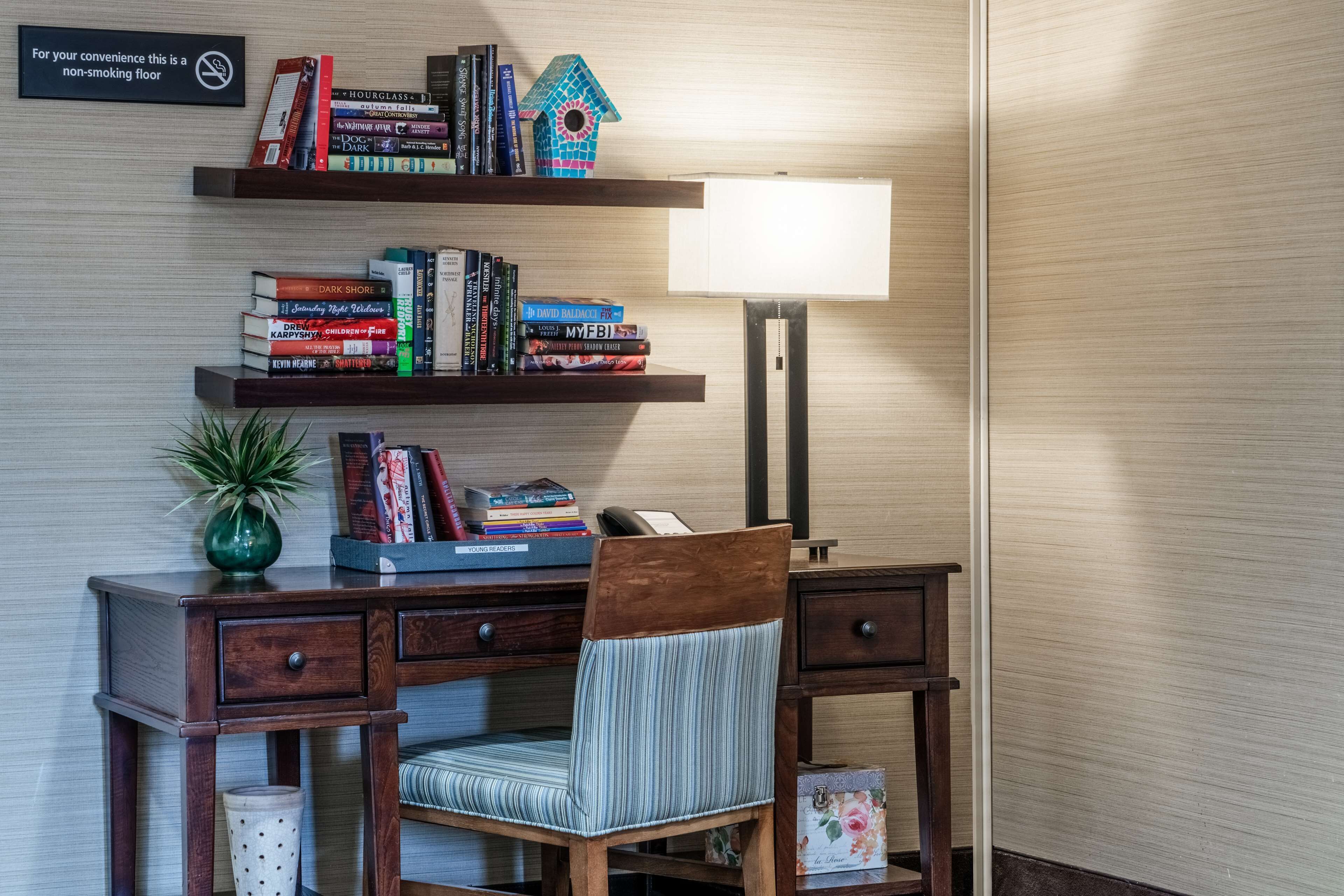 A wooden desk with a chair, a bookshelf with books, a lamp, and a sign indicating a non-smoking floor.
