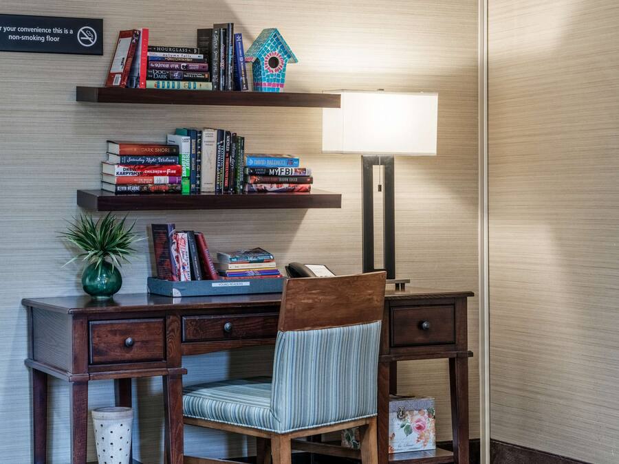 A wooden desk with a chair, a bookshelf with books, a lamp, and a sign indicating a non-smoking floor.