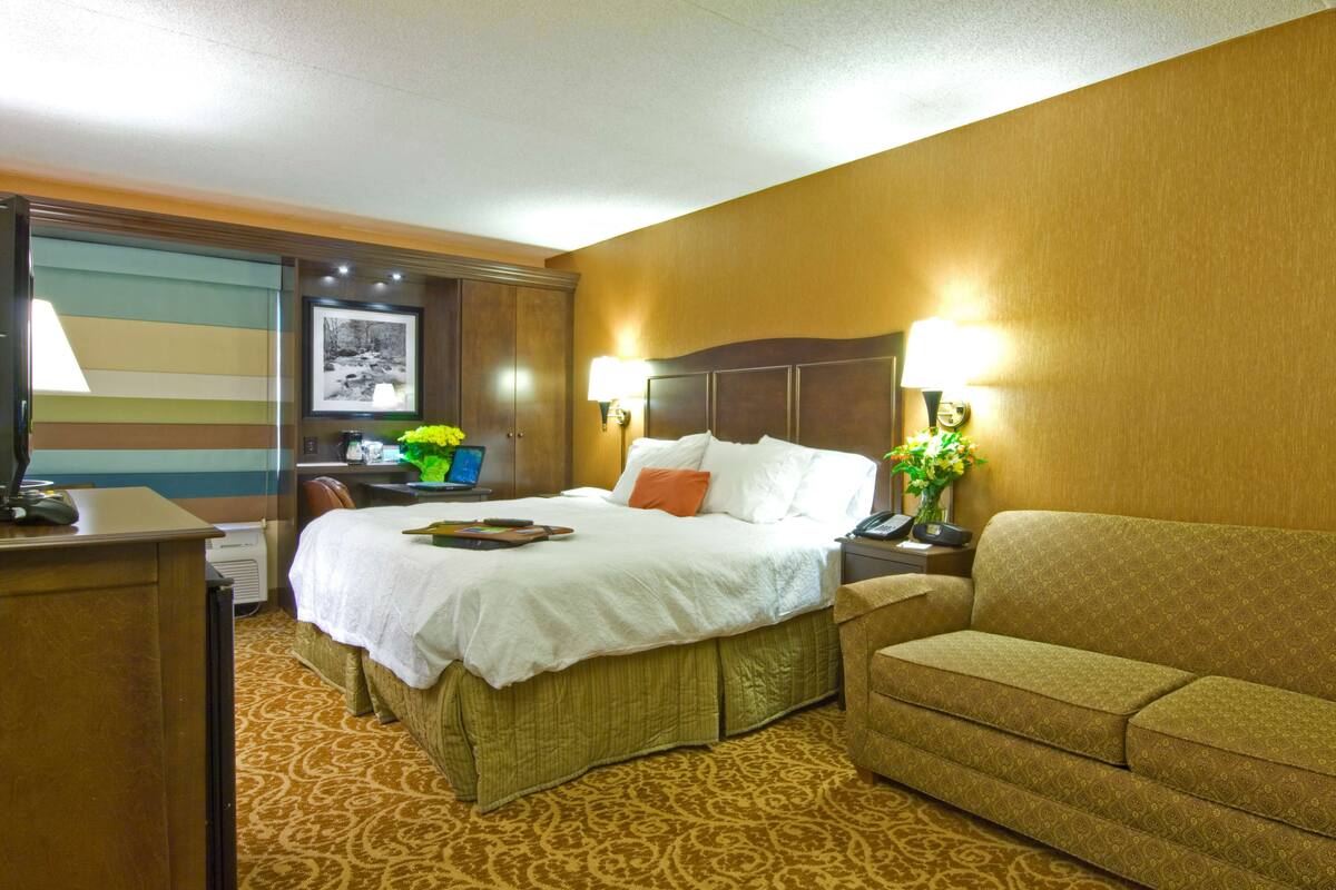 A hotel room with a bed, a desk, a chair, a sofa, and a lamp.