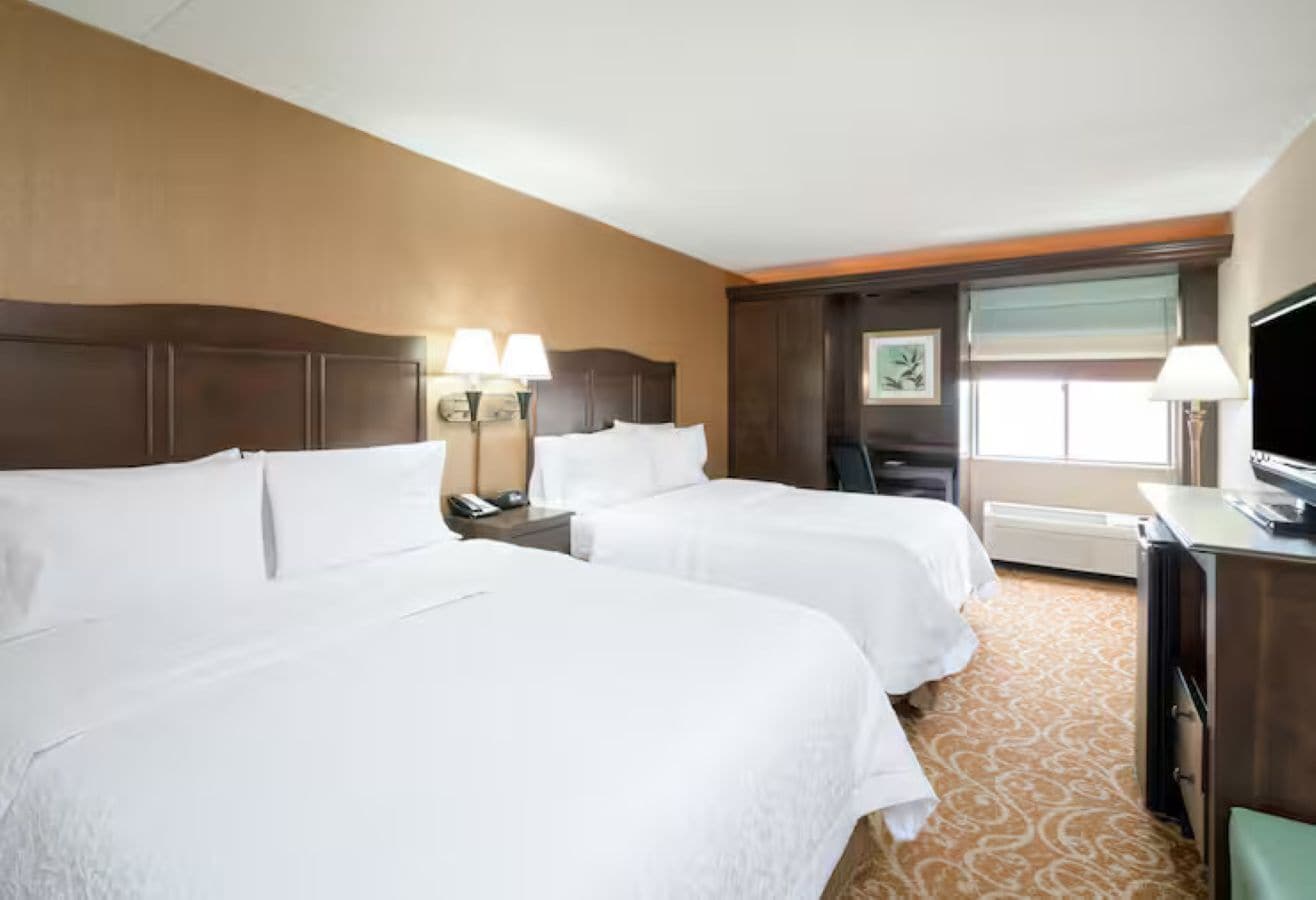 A hotel room with two beds, a desk, a television, and a window with a view.