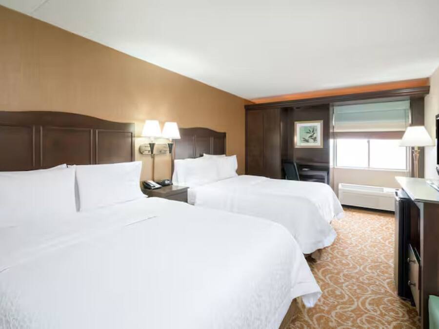 A hotel room with two beds, a desk, a television, and a window with a view.