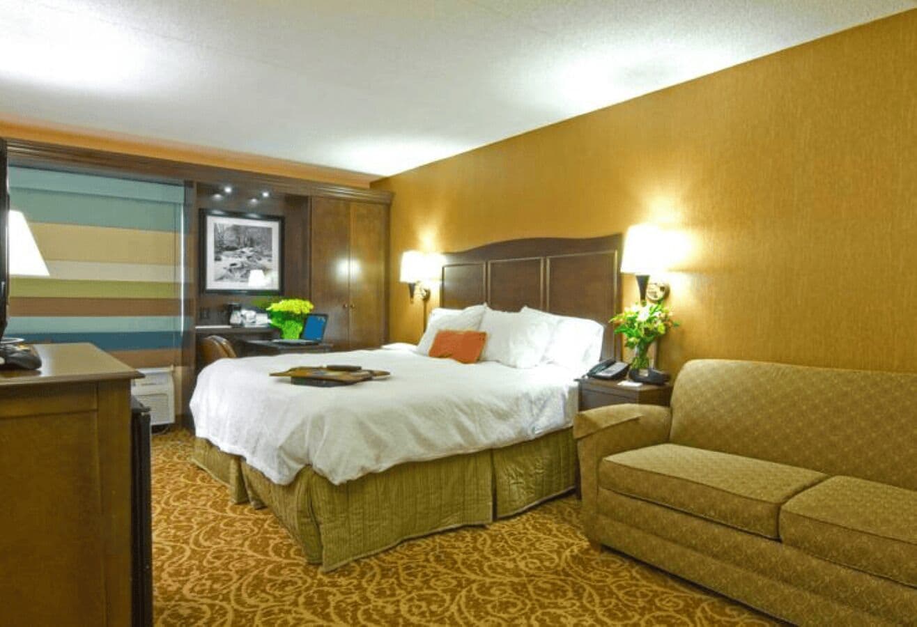 A hotel room with a bed, a desk, a sofa, and a lamp.