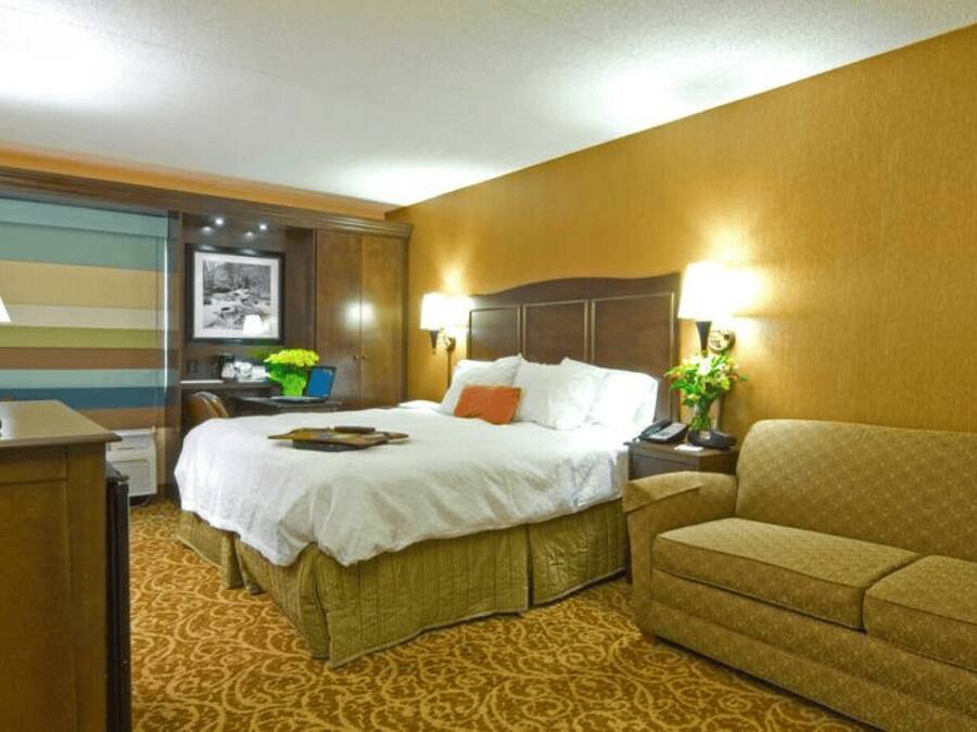 A hotel room with a bed, a desk, a sofa, and a lamp.