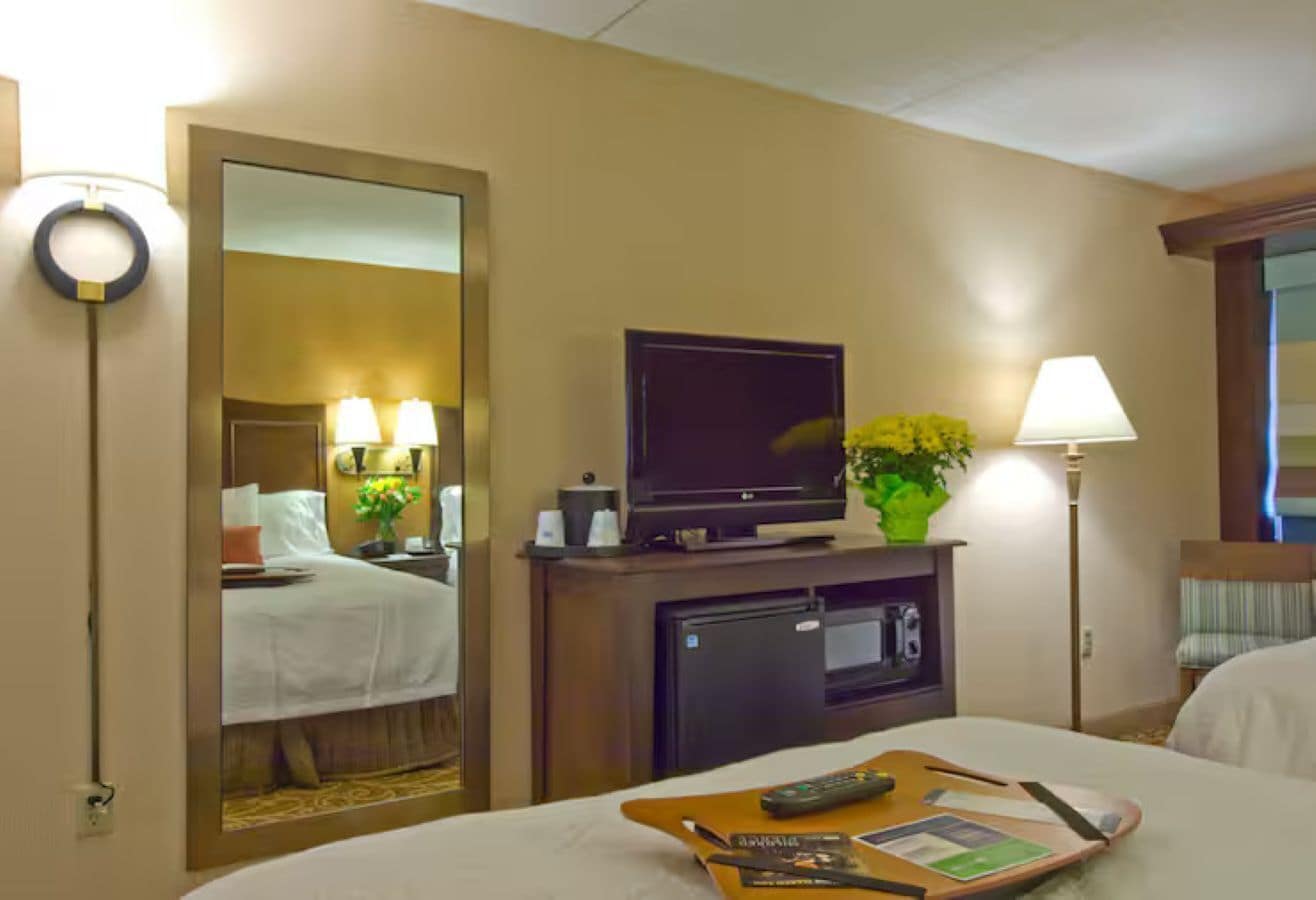 Une chambre d’hôtel comprenant un lit, une télévision, un bureau avec une lampe et un miroir.