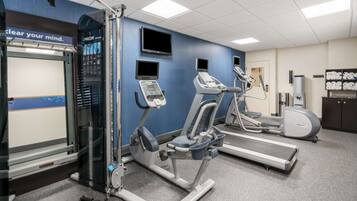 A gym with various exercise machines, a treadmill, and a wall-mounted TV.