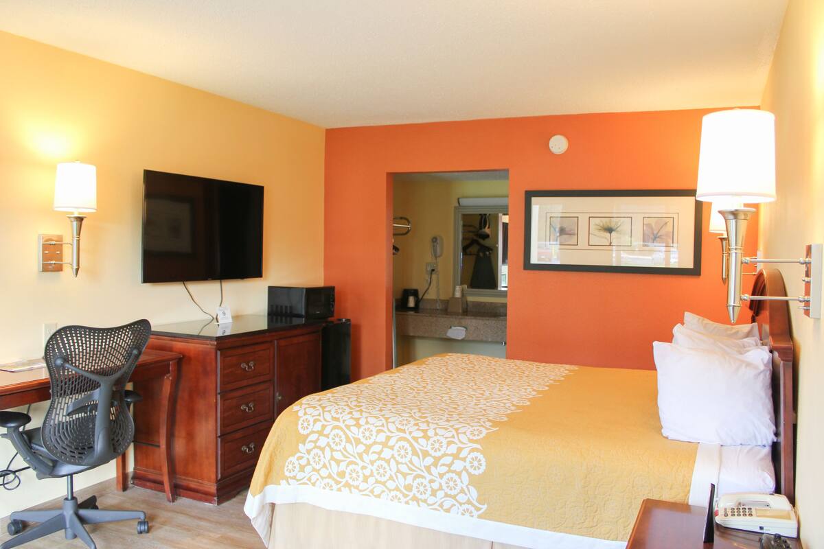A hotel room with a bed, desk, chair, TV, and a bathroom visible through an open door.