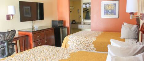A hotel room with two beds, a desk, a chair, a TV, and a bathroom visible through an open door.