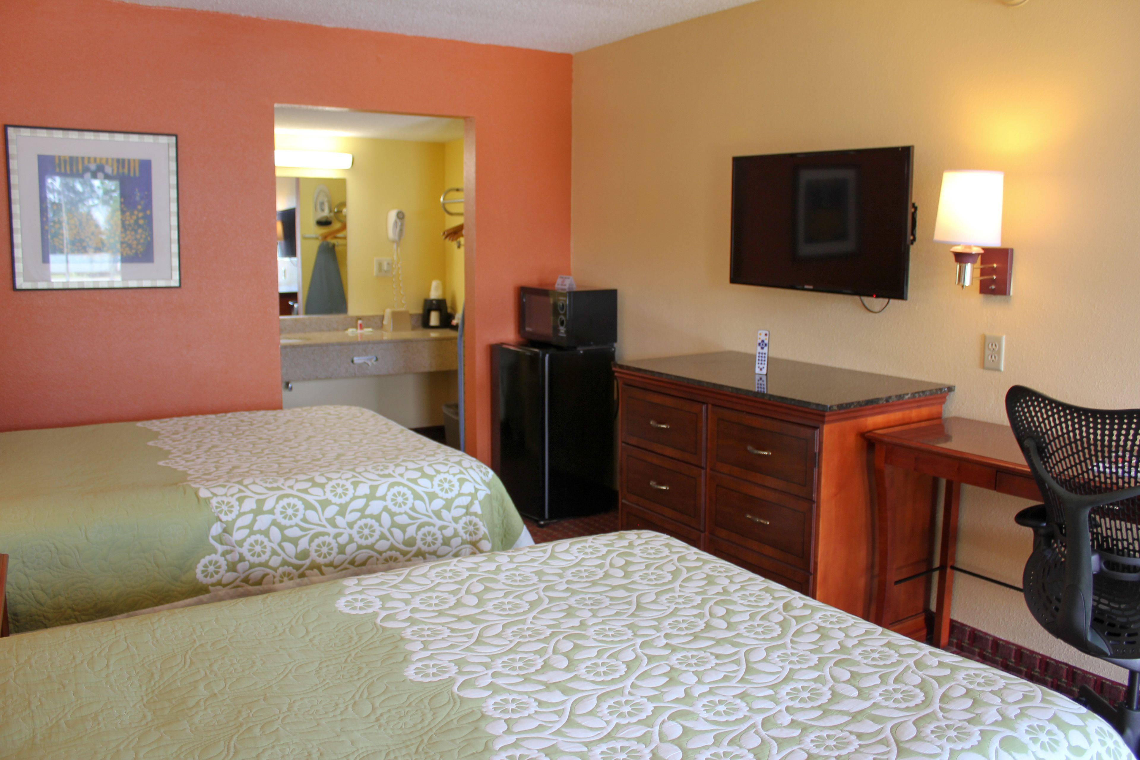 A hotel room with two beds, a desk, a chair, a television, and a bathroom visible through an open door.