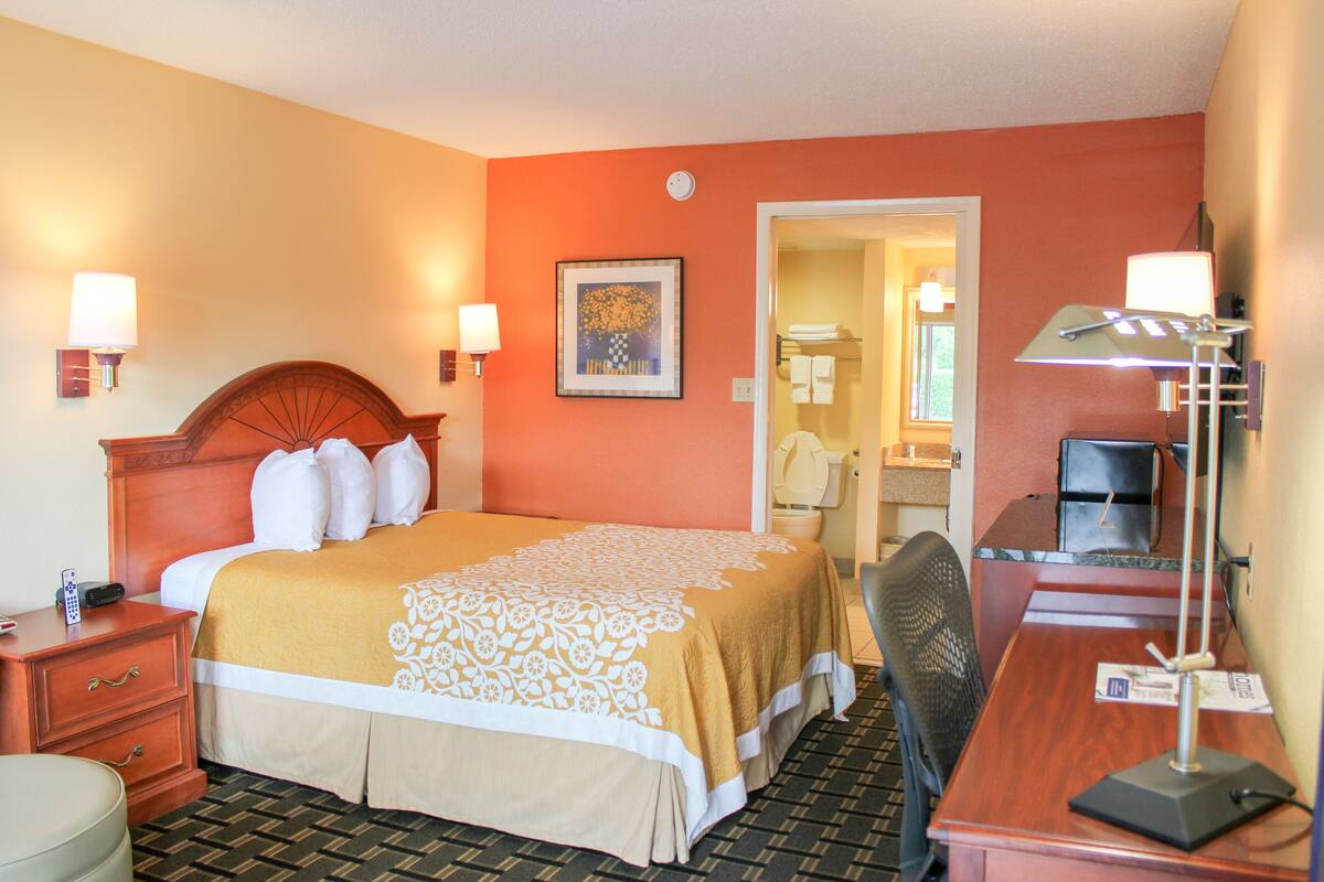 A hotel room with a bed, bedside tables, a desk, a chair, and a lamp.