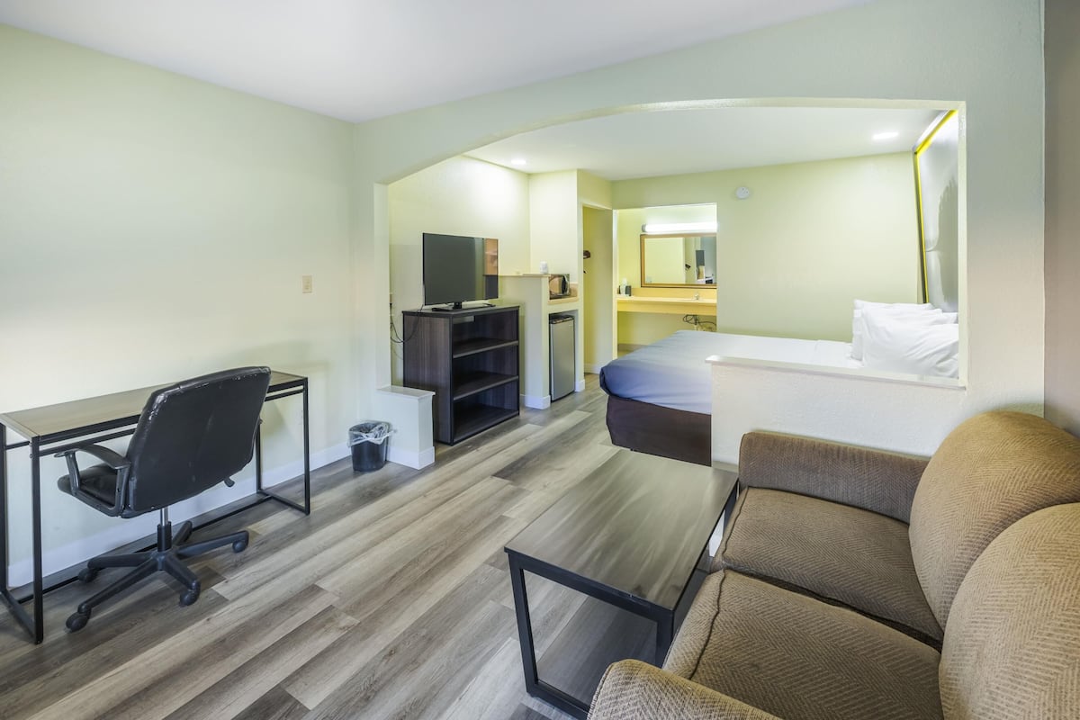 A hotel room with a desk, office chair, bed, and a small kitchenette.